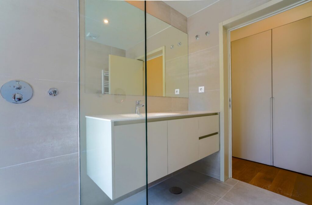 Frameless glass shower screen in a grey tiled bathroom with a white floating vanity