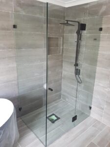 Newly installed frameless glass shower screen with matte black hinges and clamps in a grey tiled bathroom